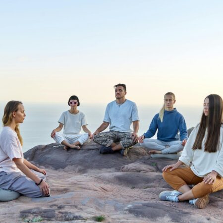 Five adults meditating outdoors on a mountain top during sunrise, promoting relaxation and mindfulness.